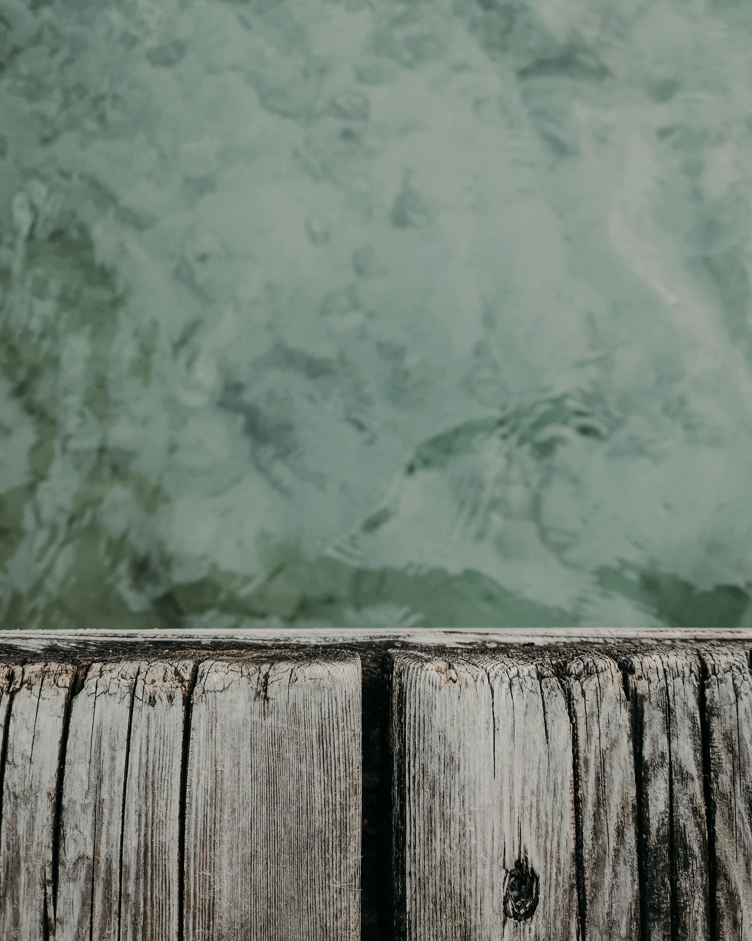 Detailed view of a weathered wooden dock meeting the tranquil surface of water, perfect for texture study.