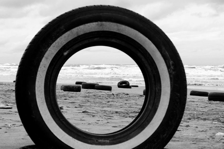 Black and white image of tires on a Mazandaran beach, Iran with crashing waves.
