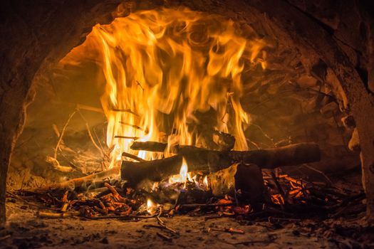 Cozy close-up of a bright fire burning in a traditional brick oven.