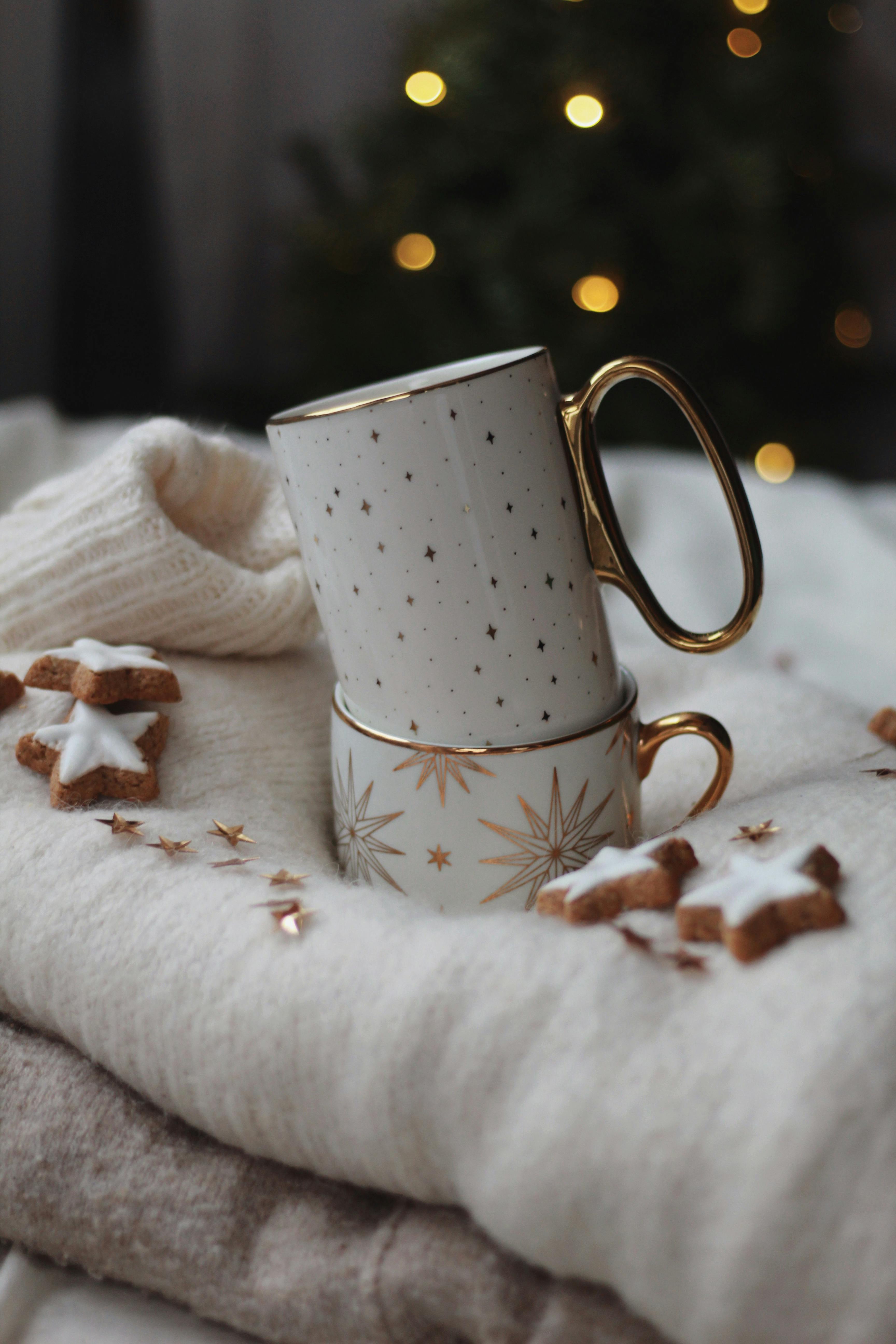 Stacked mugs with stars on cozy blankets, surrounded by Christmas cookies and soft lighting.
