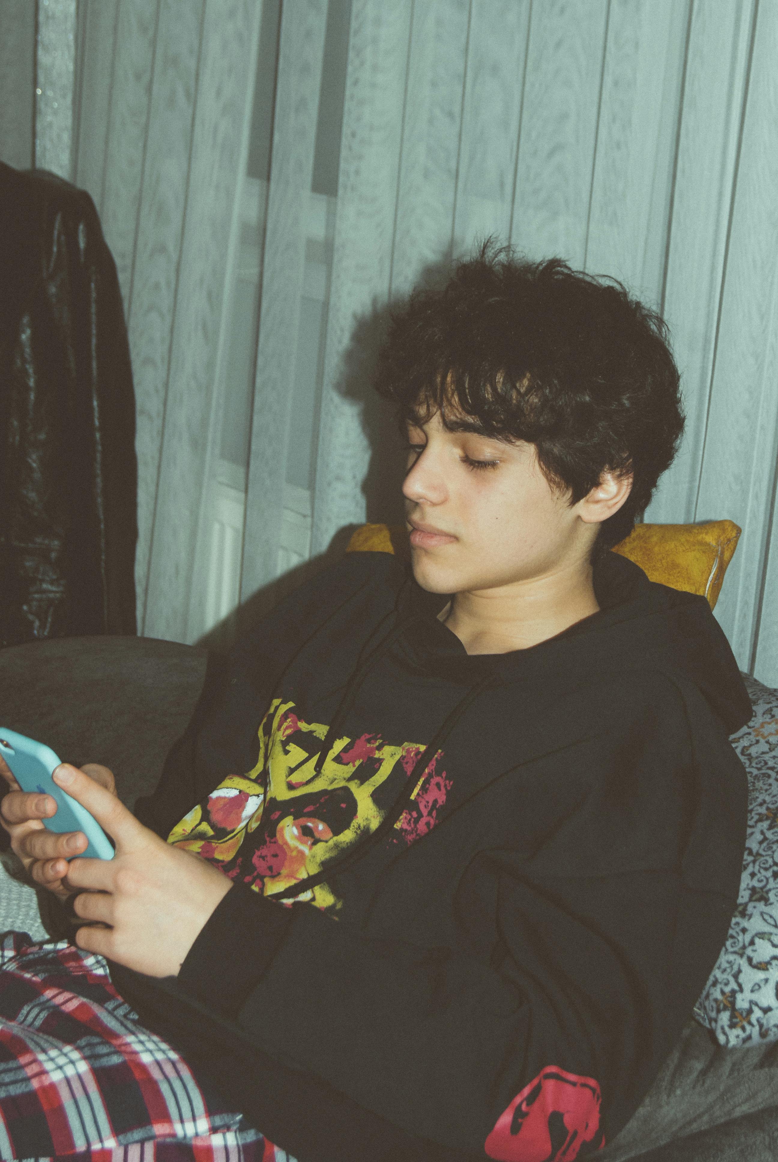 Teenage boy in casual wear using a smartphone in a cozy indoor setting.