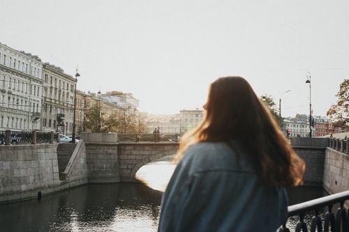 Free A woman admires the scenic view of a historic city's canal and bridge, basking in warm sunlight. Stock Photo