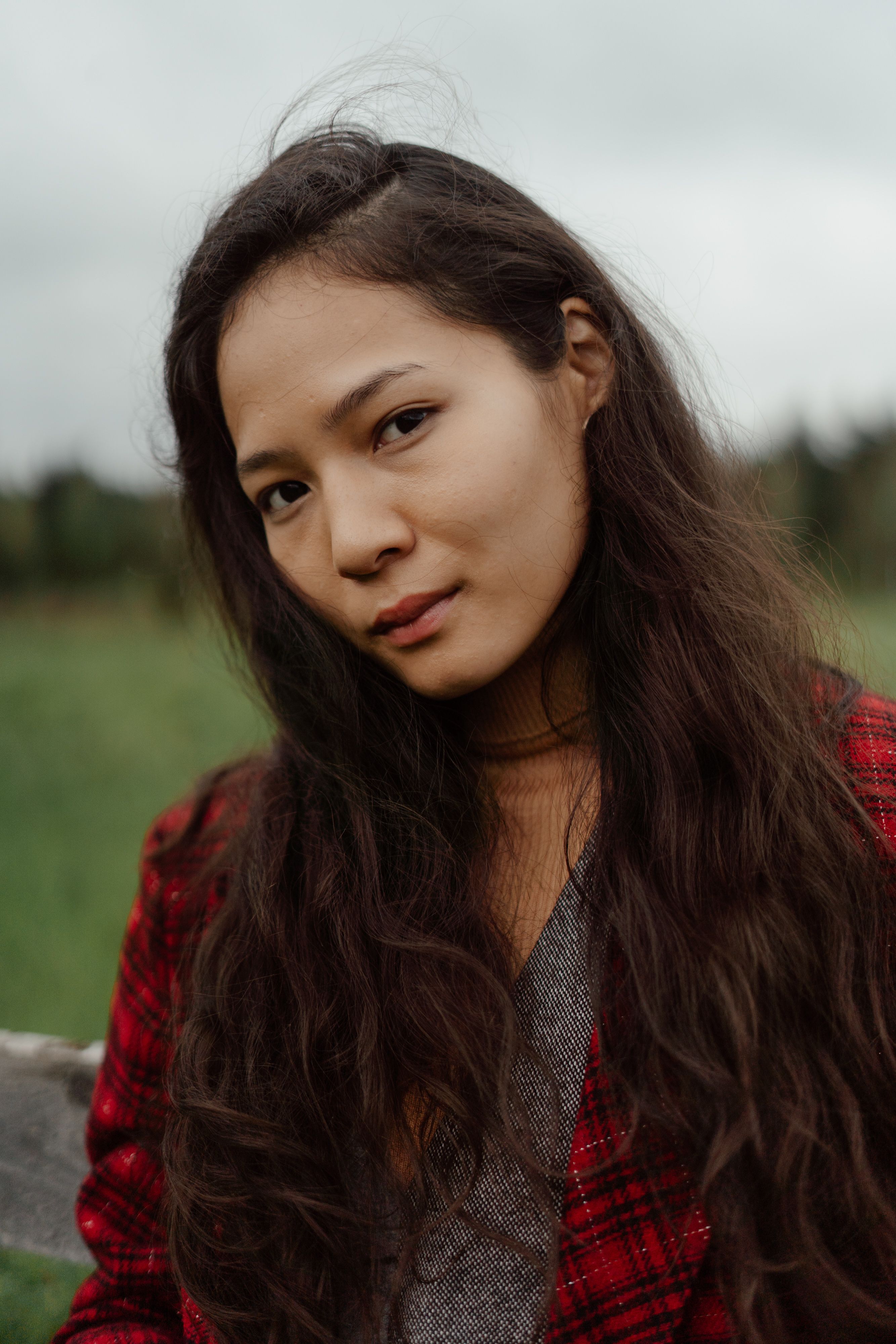 A natural light portrait of a woman wearing a plaid jacket in a serene outdoor setting with a blurred background.