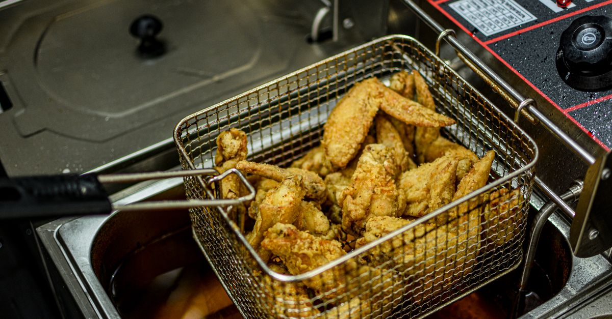 Iemand maakt de mand en lade van een airfryer schoon met een zachte spons
