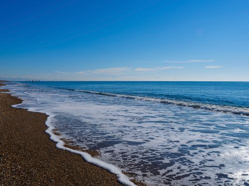 Free Serene beach scene with waves gently lapping the shore under a clear blue sky. Stock Photo