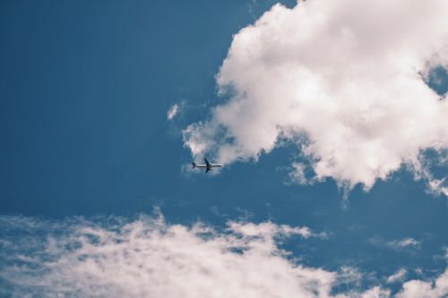 Free A scenic view of an airplane flying high in a clear blue sky with fluffy white clouds. Stock Photo