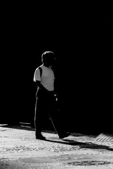 A striking black and white silhouette of a man walking against a dark background.