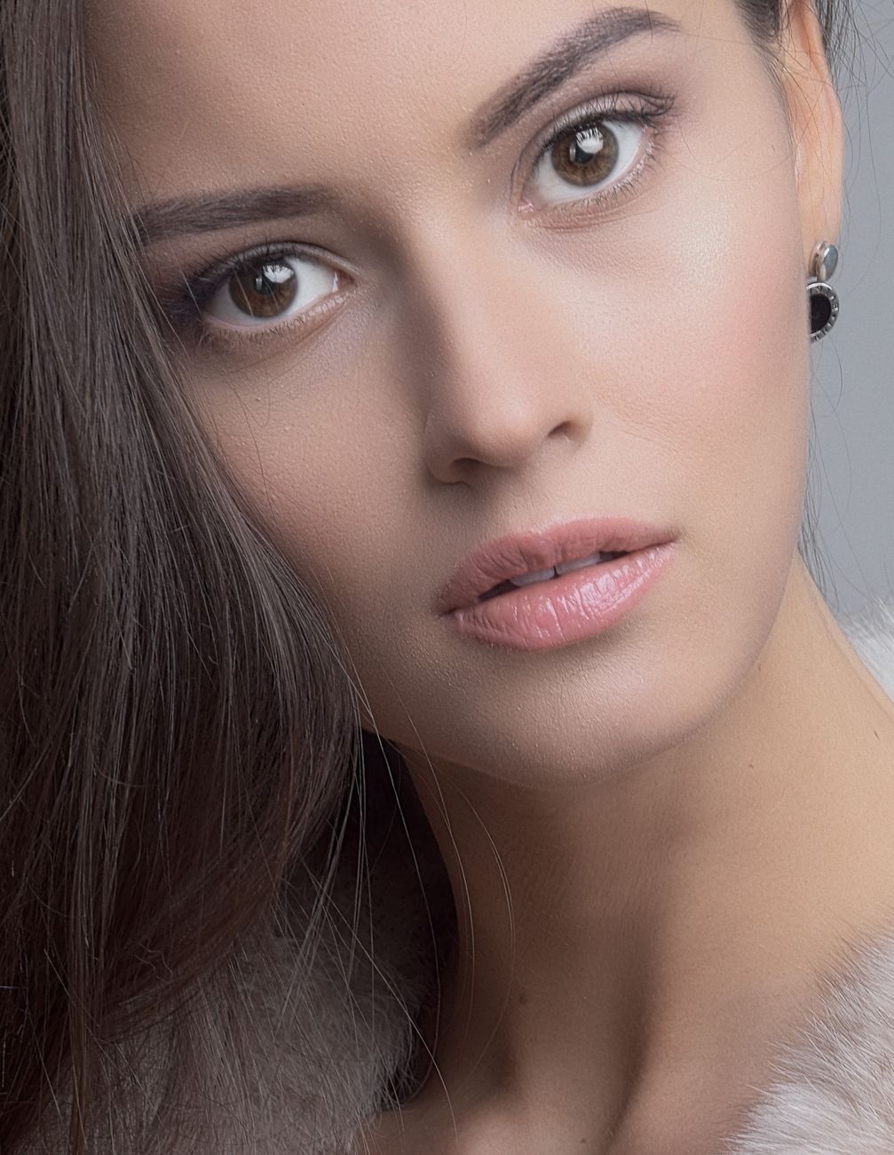 Close-up portrait of an elegant woman with long hair and neutral makeup featuring pink lipstick.