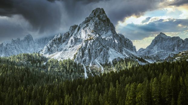 Spectacular view of a snow-dusted mountain peak surrounded by lush green forest under a moody sky.