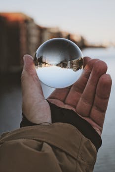 Close-up of a hand holding a glass ball reflecting a city's inverted skyline.