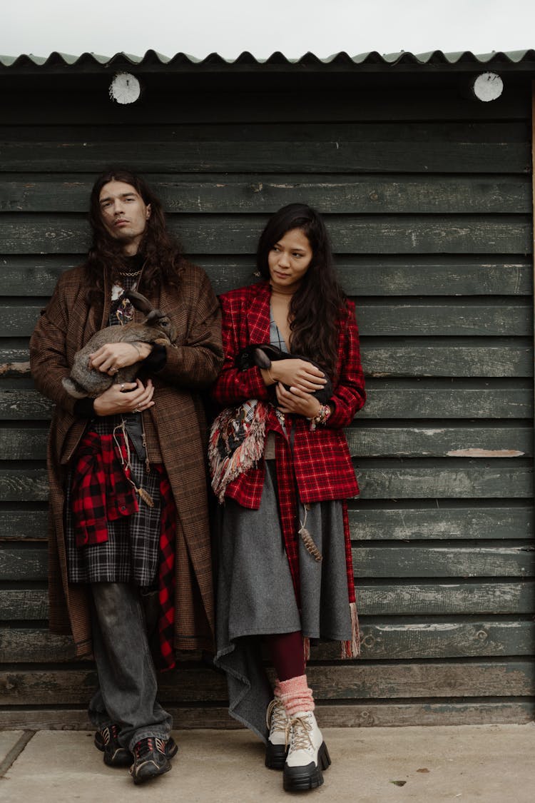 Man And Woman Leaning On Wooden Wall While Carrying Rabbits 