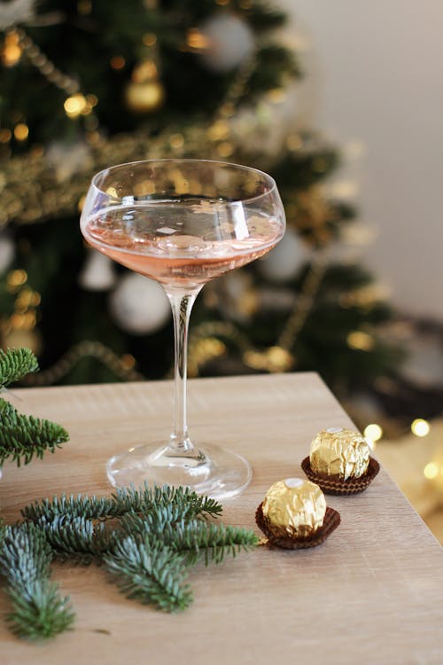 A Glass of Wine, Chocolates and Pine Leaves on a Wooden Table