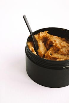 Close-up of a natural exfoliating face scrub in a black jar with a spoon, ideal for skincare routines.