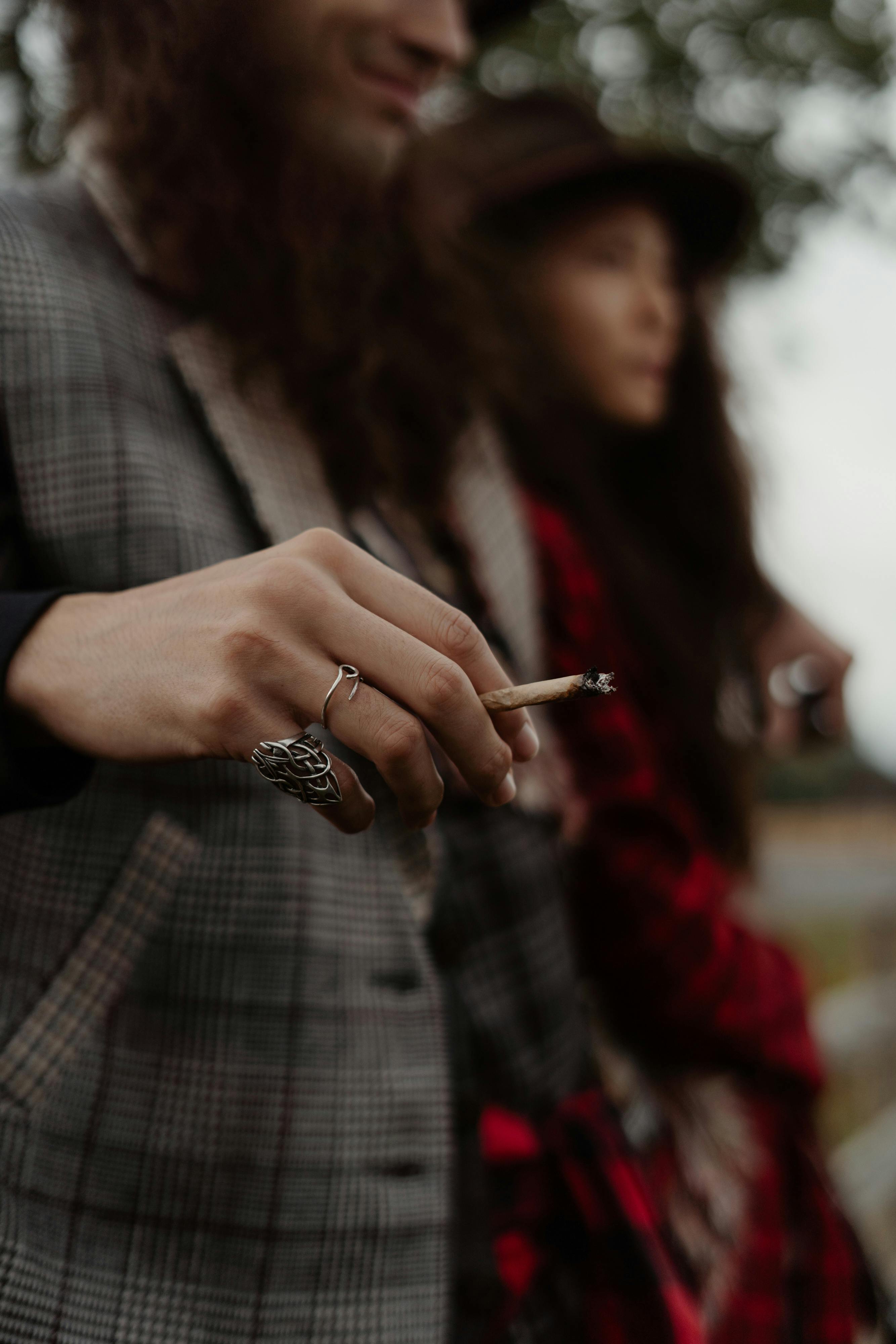 man in gray and black plaid coat holding cigarette stick beside a woman