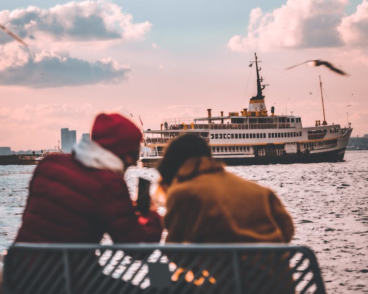 People Sitting On Bench Near Sea And Talking