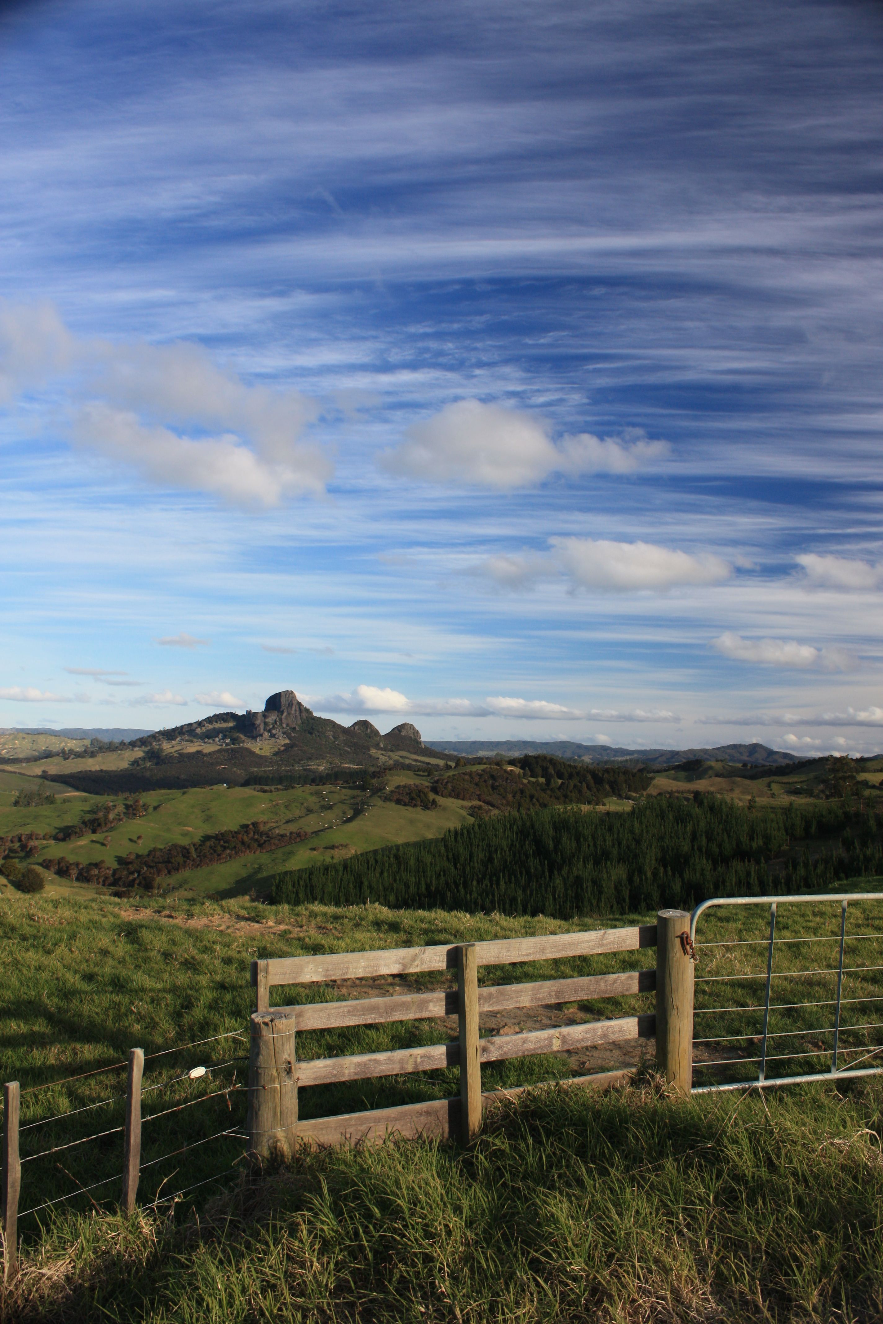 A scenic countryside landscape featuring a wooden fence, hills, and a vibrant blue sky.