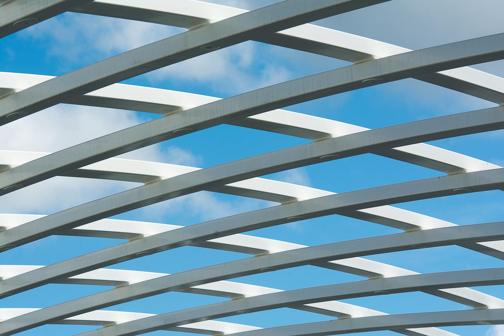 Sleek white steel beams form a modern geometric pattern against a bright blue sky.