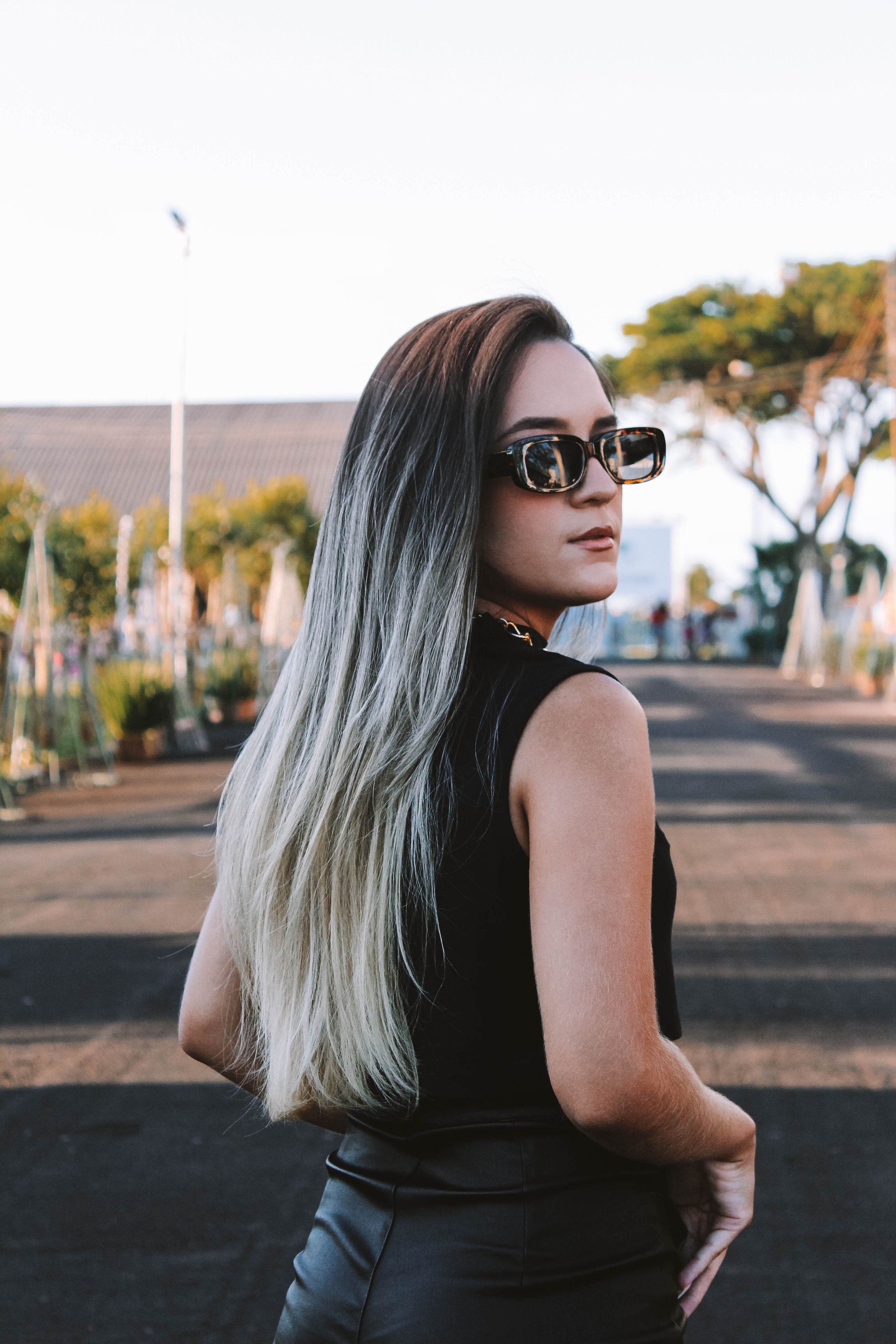Uma mulher fashion com cabelo ombre e óculos de sol, em pé ao ar livre, com um olhar confiante.
