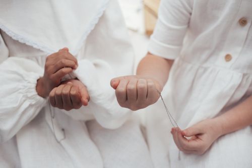 Free Two girls in white dresses delicately hold jewelry pendants, showcasing friendship. Stock Photo