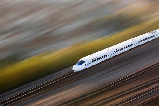 A sleek white high-speed train traveling at top speed, captured with a motion blur effect.