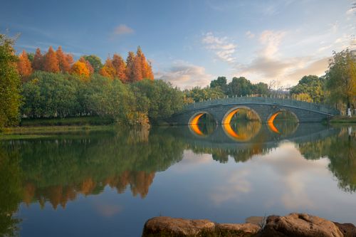 Free A peaceful scene of an arched bridge reflecting in a pond during autumn. Stock Photo