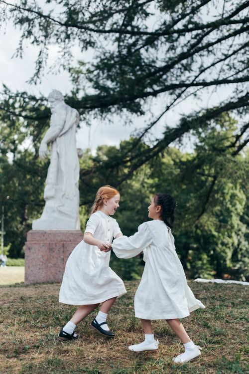 Free Two girls in white dresses playing near a classical statue in a park Stock Photo