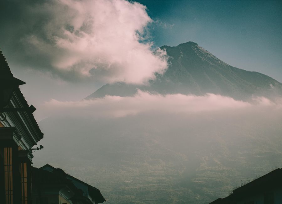 Dramatic view of a volcano with clouds over Ciudad de Guatemala's architecture.