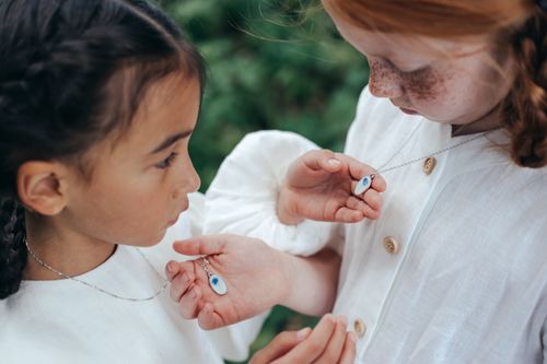 Free Two young girls admiring each other's necklaces in a park setting, showcasing friendship and innocence. Stock Photo