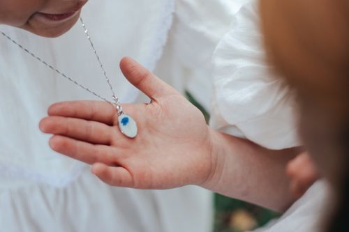 Free Close view of a child's hand holding a silver necklace with a blue pendant. Stock Photo