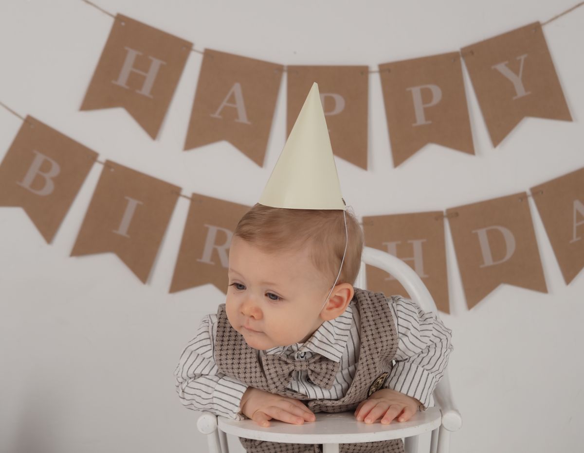 Baby with birthday hat in a high chair with banner