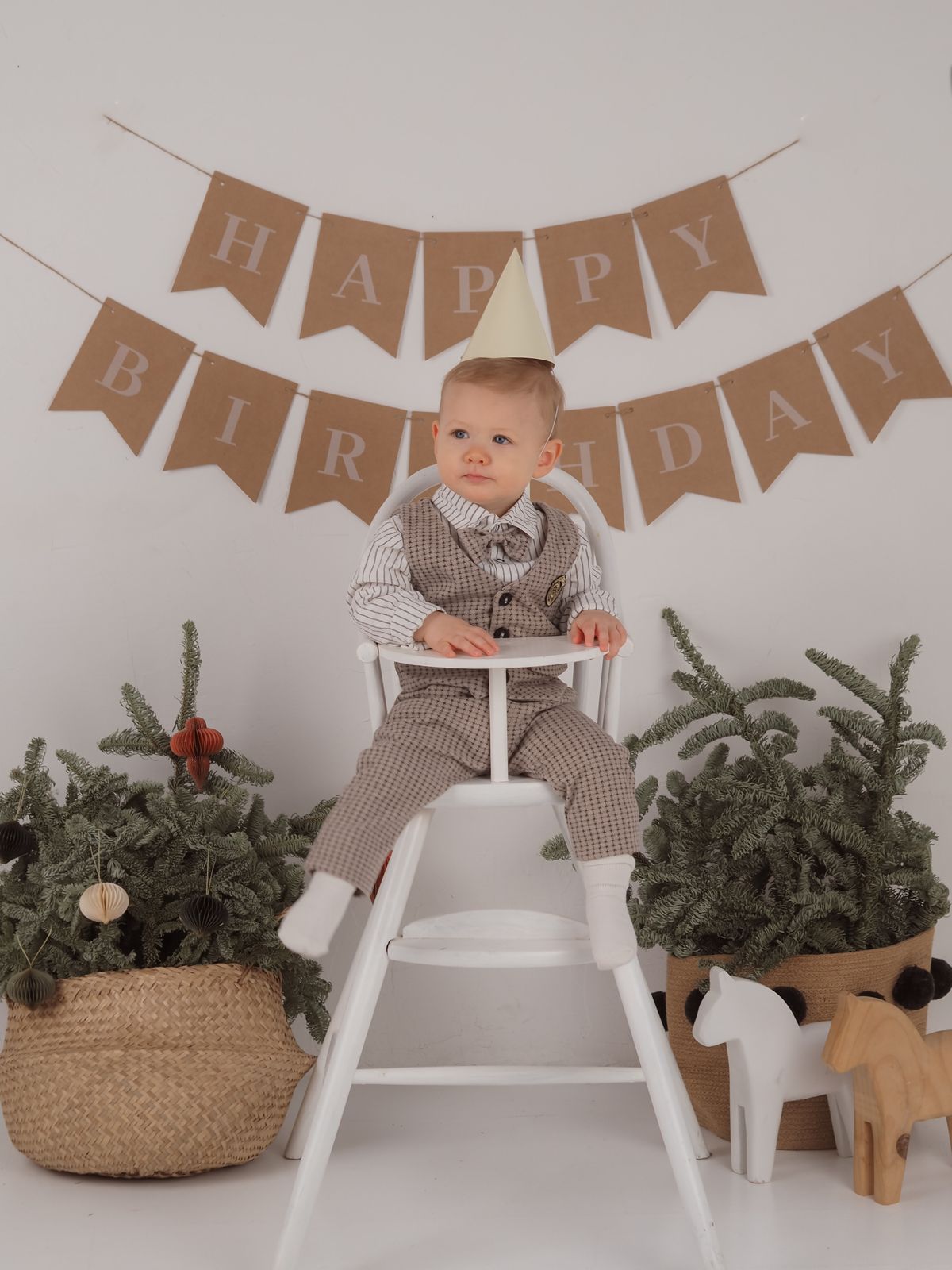 A young boy wearing a party hat celebrates his birthday in a high chair with decorations. Stock Photo.