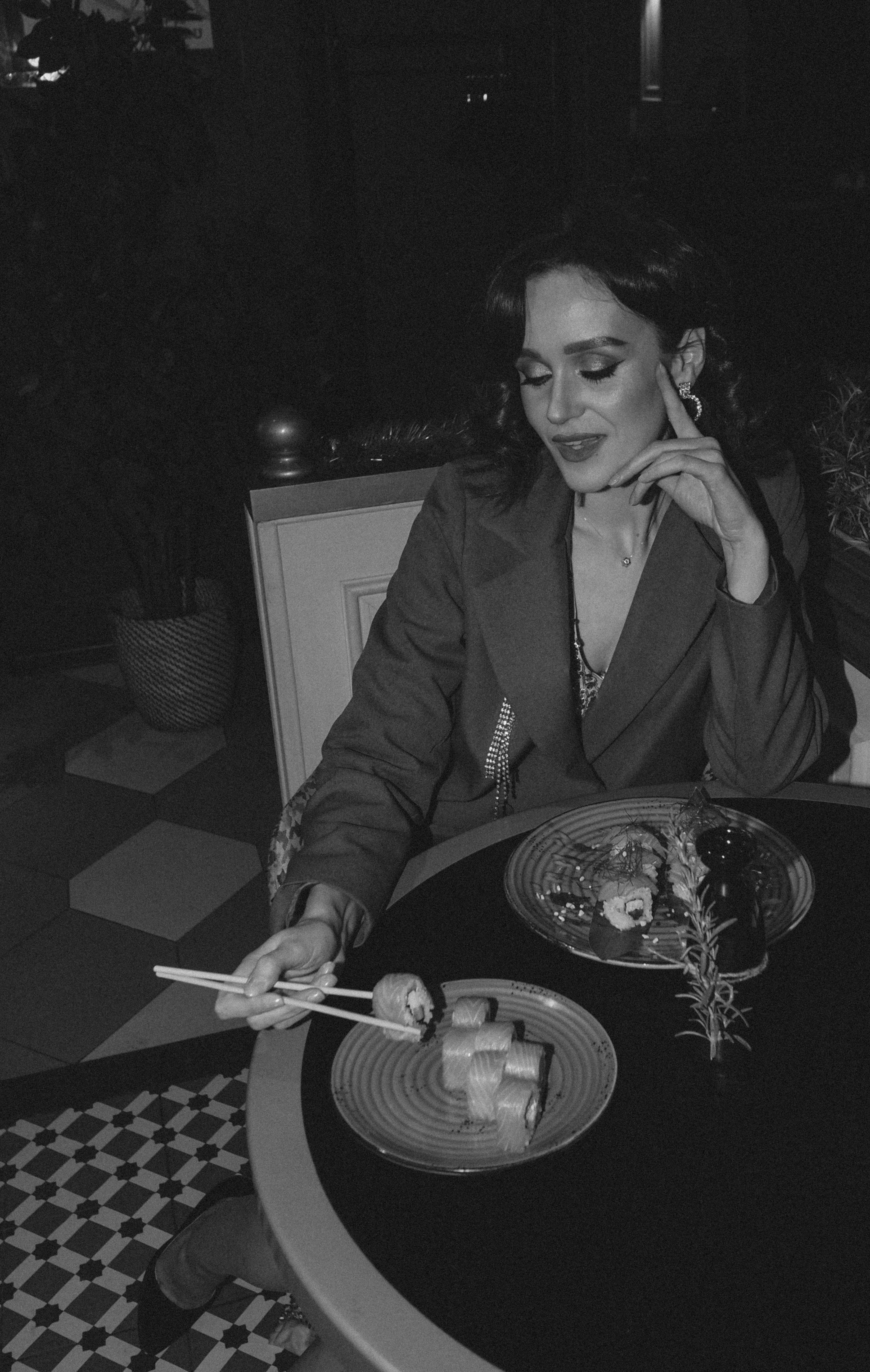 Stylish woman enjoys sushi in a chic restaurant setting using chopsticks.