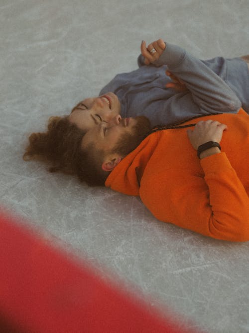 Free Man in Orange Hoodie Laying Beside Woman in Gray Hoodie Stock Photo