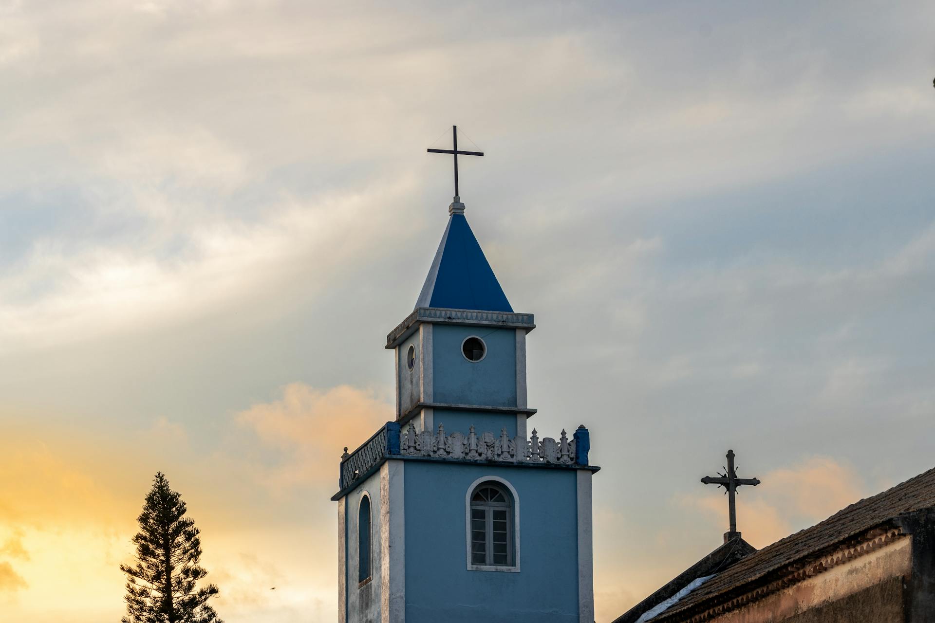 A serene view of a blue church tower with a cross at sunset, capturing the essence of sacral architecture.