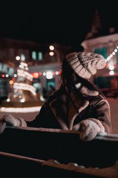 A woman in cozy winter attire enjoys a night at a festive outdoor market with colorful lights.