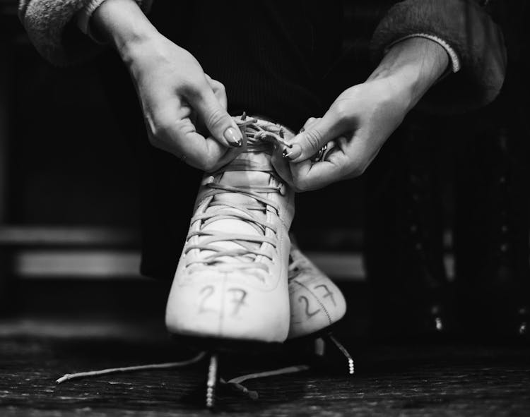 A Grayscale Of A Person Tying An Ice Skate