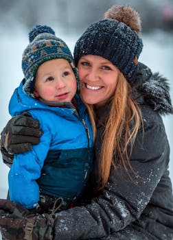 A cheerful mother and child embrace warmly amidst a snowy winter backdrop.
