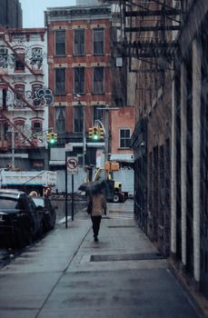 Person walking on a wet city sidewalk under an umbrella during rainfall.
