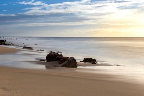 Free Calm beach landscape with smooth waves over rocks at sunrise, creating a peaceful scene. Stock Photo