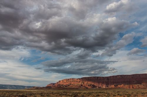 Free Expansive view of dramatic clouds over a rugged desert with red rock formations. Stock Photo