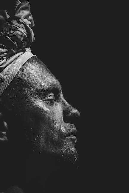 Artistic black and white profile portrait of a man with eyes closed on black background.