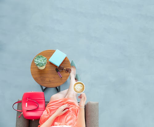 女人穿着桃子裙子坐在沙发上的椅子上，拿着一杯咖啡