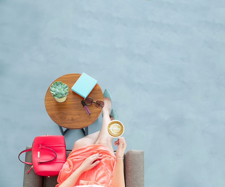 A woman in a peach dress enjoying a coffee with latte art indoors, featuring a stylish setup.