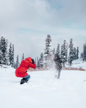 Person in Red Jacket and Black Pants Riding on Black Snowboard on Snow Covered Ground during
