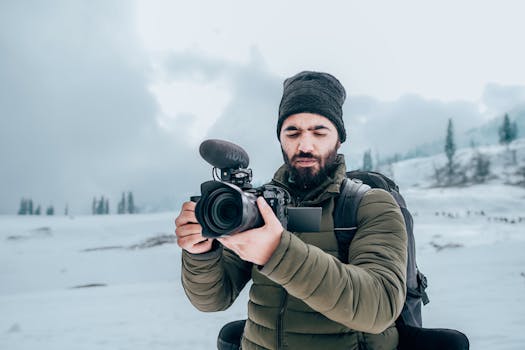 A bearded man with a camera captures winter scenery in Gulmarg, showcasing snow and travel photography.