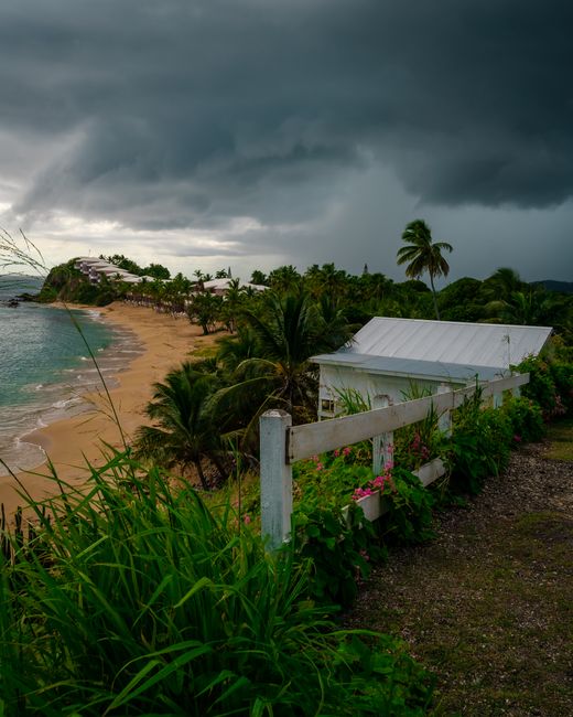 Dark storm clouds loom over a serene beach in Antigua, creating a dramatic tropical scene. - Barbados Weather by Month: Rainy Season & Hurricane Risk