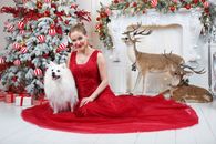 Woman in Red Sleeveless Dress Sitting Beside White Long Coated Dog on White Bed