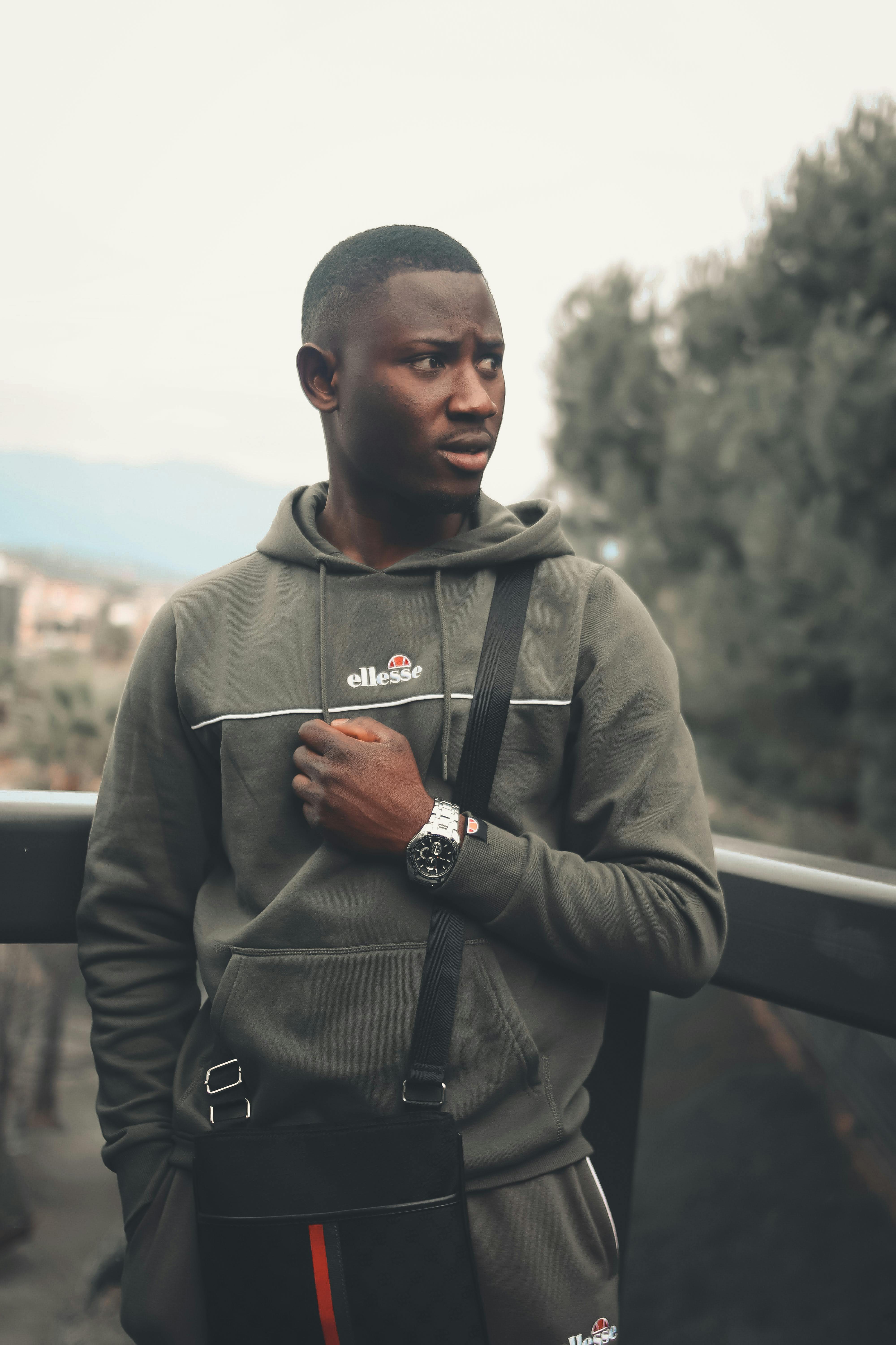 Black man in a gray hoodie posing outdoors with a thoughtful expression.