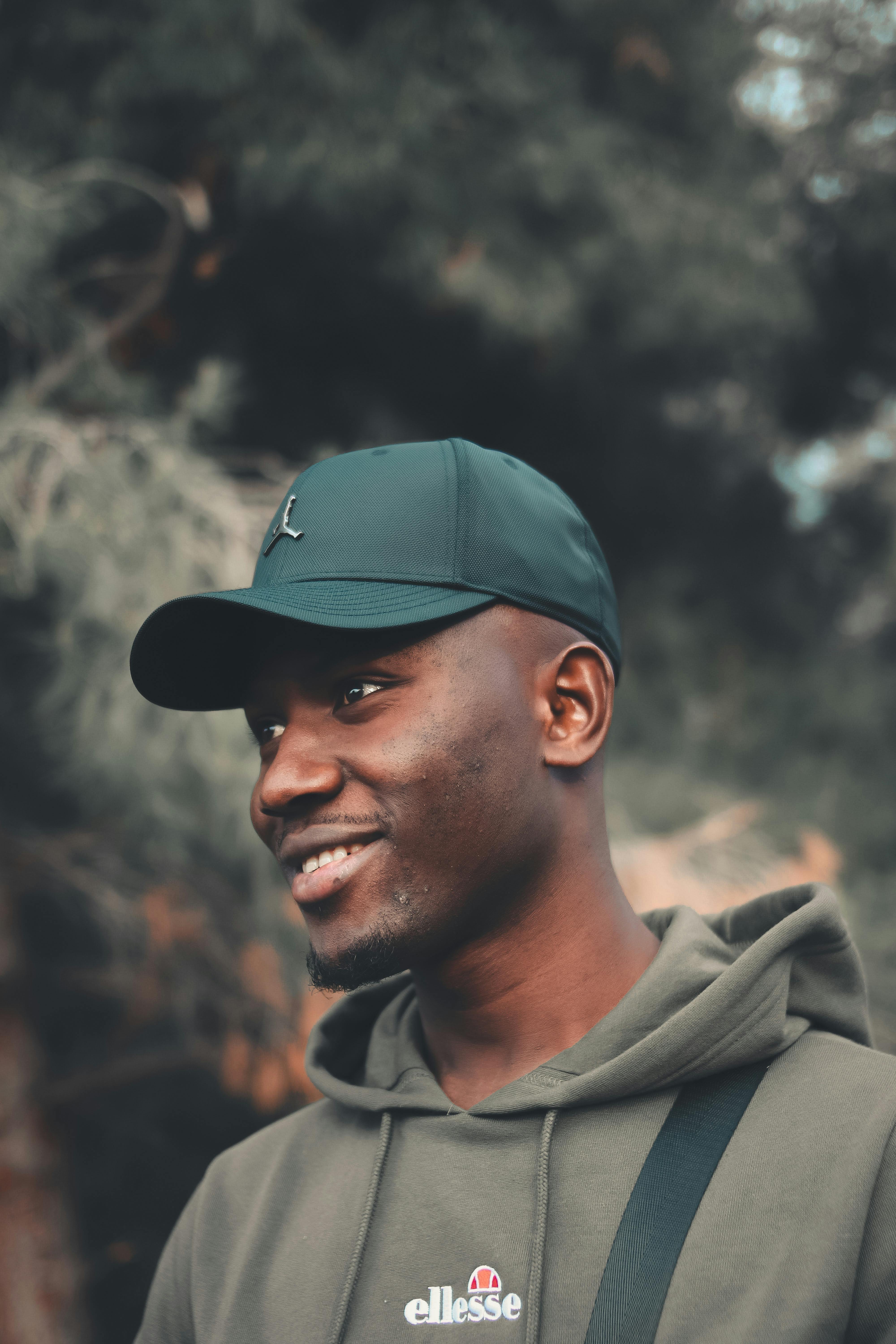 A smiling man in a hoodie and cap enjoying the outdoors.