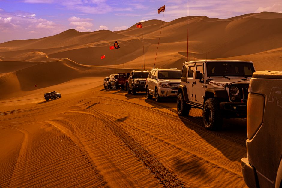 Conduite d'un 4x4 d'expédition sur piste sablonneuse A convoy of off-road vehicles navigating through vast desert dunes during the day.